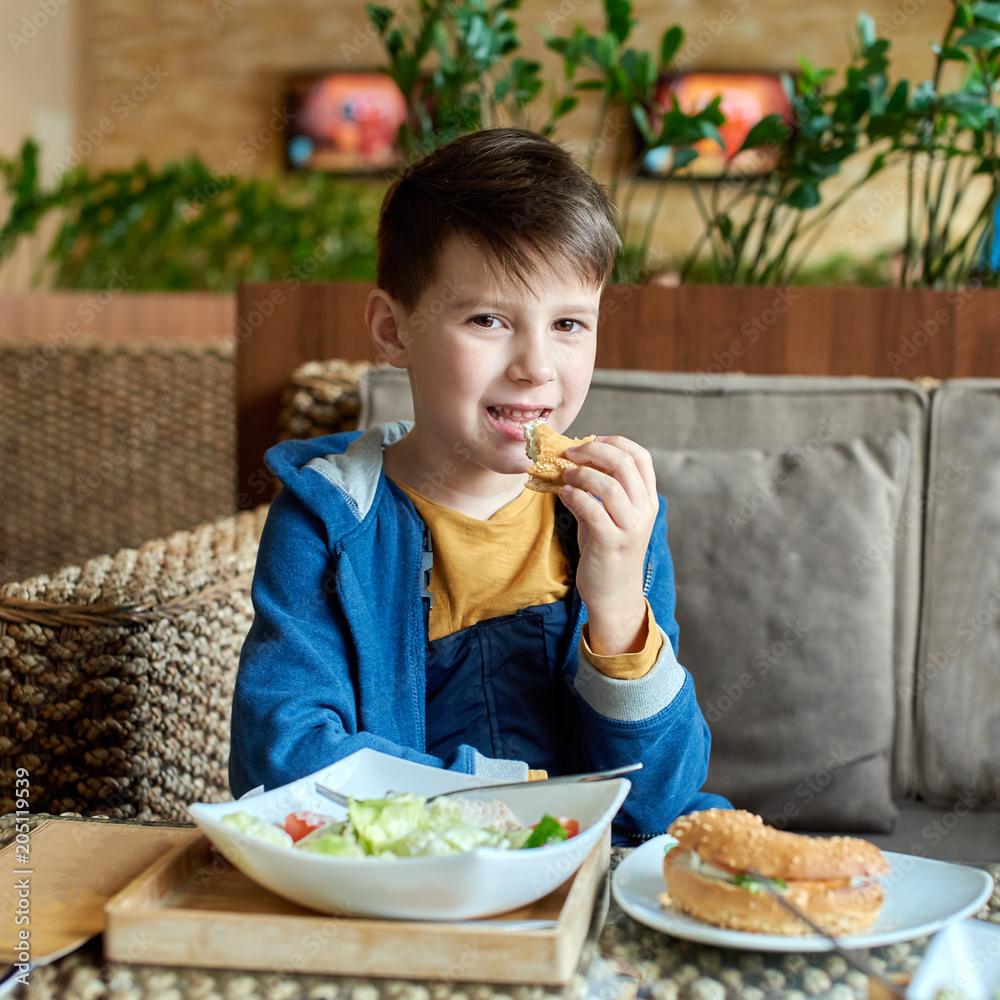 Cheerful Caucasian boy enjoying a Caesar salad and a burger at a restaurant. His smiling into the camera. Cheerful Caucasian boy enjoying a Caesar salad and a burger at a restaurant. His smiling into the camera.