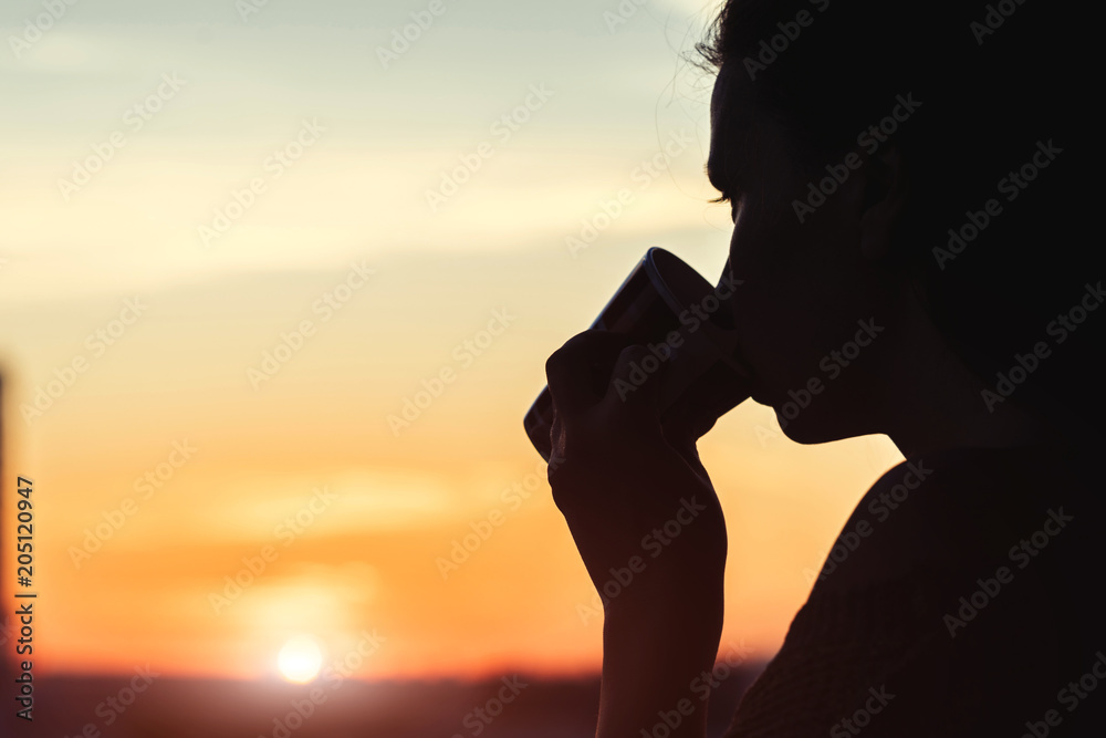 Silhouette of girl with a cup of coffee in the morning. View on the town from above