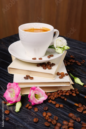 Cup of coffee on top of pile of books with coffee beans and flowers scattered on the table
