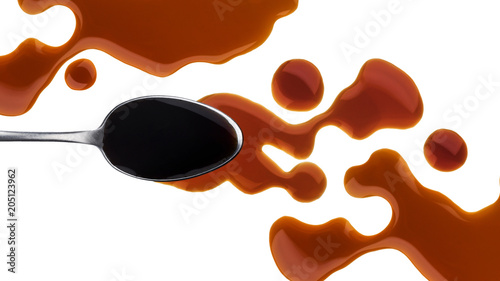 Spilled soy sauce with spoon isolated on white background