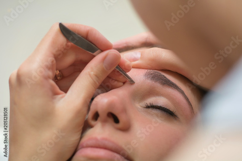 Beautiful young woman gets eyebrow correction procedure. Young woman painting her eyebrows in beauty saloon. close-up of a young woman plucking eyebrows with tweezers photo