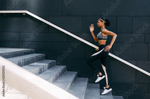 Side view of woman in sportswear running up the steps in the city. Female athlete doing workout at the day.
