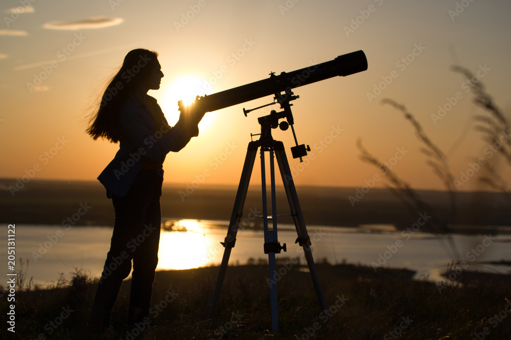 Silhouette of young woman looking view through the telescope at summer sunset