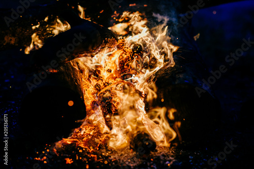 Burning wood at night. Campfire at touristic camp at nature in mountains. Flame amd fire sparks on dark abstract background. Cooking barbecue outdoor. Hellish fire element. Fuel, power and energy.