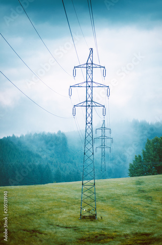 High voltage towers in a middle of forests and meadow. Electricity pylon with dark atmosphere in a nature. Rainy day. Power transmition towers. photo