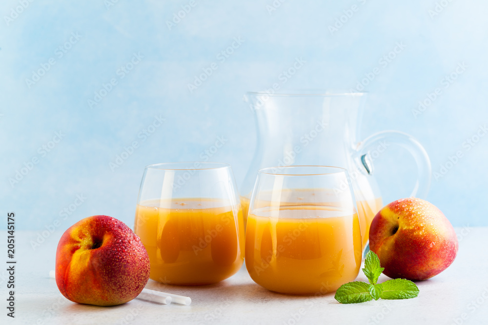 peach juice in glasses and a decanter and fresh peaches with leaves on a table. blue background. copy space peach juice in glasses and a decanter and fresh peaches with leaves on a table. blue background. copy space