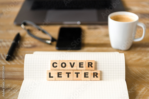 Closeup on notebook over wood table background, focus on wooden blocks with letters making COVER LETTER words