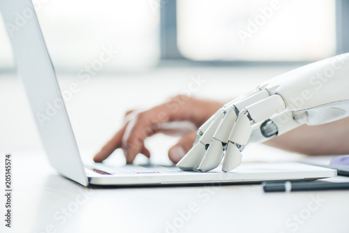 selective focus of human and robot hands typing on laptop at workplace photo