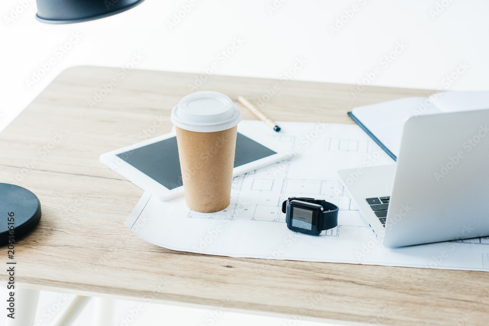 disposable coffee cup, digital tablet, smartwatch, laptop and blueprint on wooden table disposable coffee cup, digital tablet, smartwatch, laptop and blueprint on wooden table