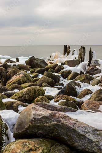 Jetty Pillars and Rocks Covered witn Snow in a Cloudy Winter Day with a Few Sun Beams Shining on Them