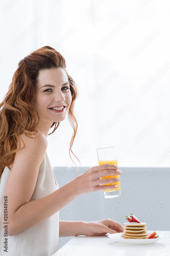 smiling young woman with orange juice and pancakes with strawberry for breakfast looking at camera smiling young woman with orange juice and pancakes with strawberry for breakfast looking at camera