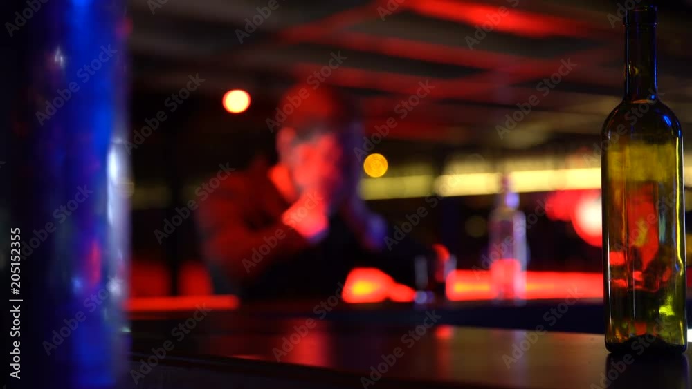 Depressed man drinking whiskey alone in nightclub, thinking over problems