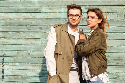 fashion couple in glasses with glasses in green clothes posing on blue wooden wall
