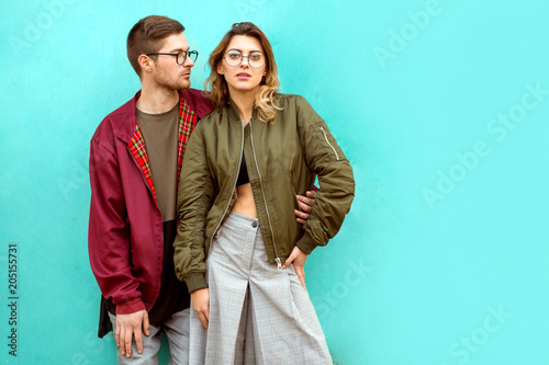 fashion couple in their glasses with burgundy clothes posing on a blue wall