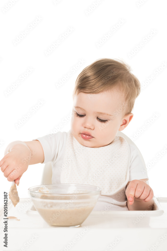 baby boy eating porridge by spoon and sitting in highchair isolated on white background baby boy eating porridge by spoon and sitting in highchair isolated on white background