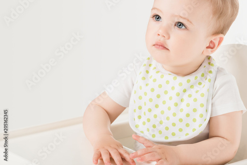 portrait of baby boy in bib sitting in highchair isolated on white background