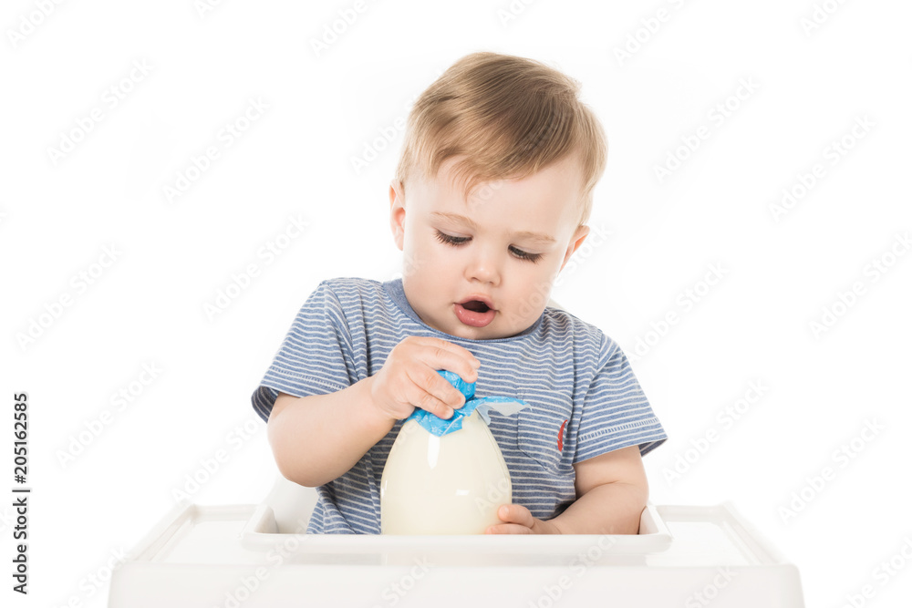 little boy trying to open bottle of milk and sitting in highchair isolated on white background little boy trying to open bottle of milk and sitting in highchair isolated on white background