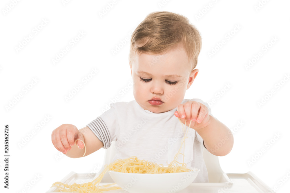 adorable child eating spaghetti by hands and sitting in highchair isolated on white background adorable child eating spaghetti by hands and sitting in highchair isolated on white background
