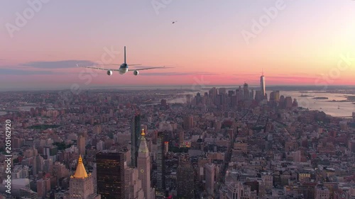 AERIAL, CLOSE UP: Large commercial plane flies over breathtaking downtown of New York at spectacular sunset. Beautiful shot of tall urban buildings stretching out into the stunning evening horizon.