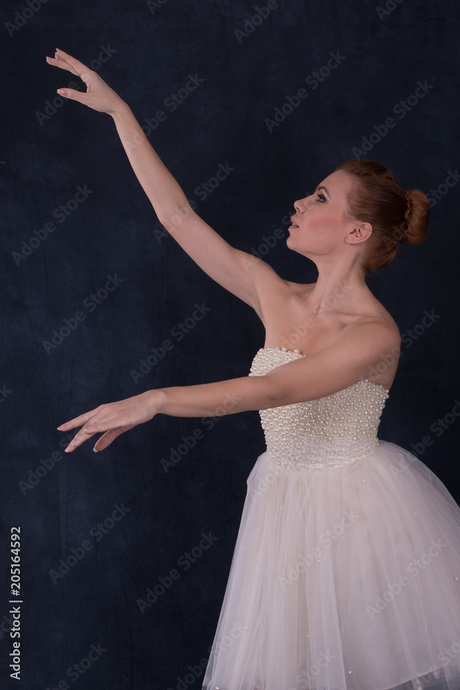 the ballerina wearing a classical white dress dances on a dark background in studio