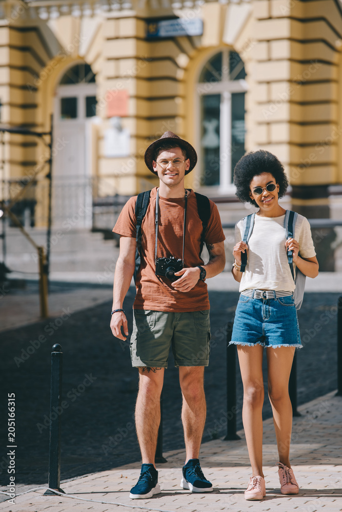 couple of young tourists with camera and backpacks standing on street couple of young tourists with camera and backpacks standing on street