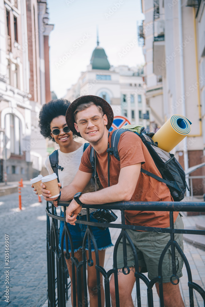 happy young interracial couple of travelers with paper cups of coffee