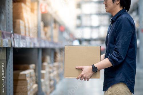 Young Asian man carry cardboard box between row of shelves in warehouse, shopping warehousing or working pick and packing concepts
