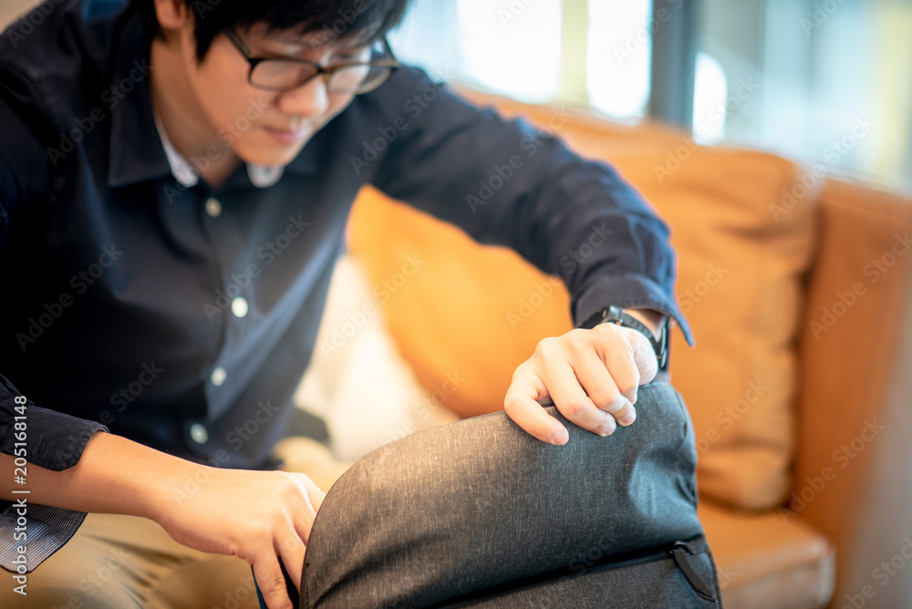 Young Asian businessman opening his bag while sitting on sofa in living room. Urban lifestyle concept