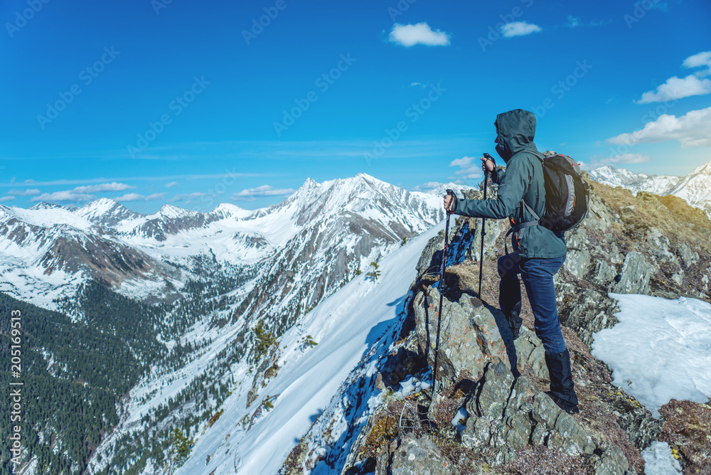 Hiker with trekking poles stands in the snowy mountains at the foot of the peak. Concept of travel and achieve the goal