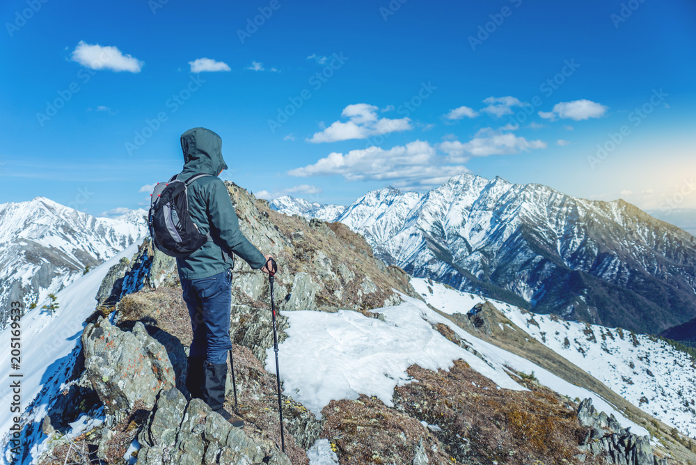 Hiker with trekking poles stands in the snowy mountains at the foot of the peak. Concept of travel and achieve the goal