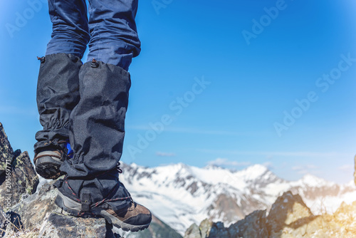 Man in Hiking boots stands on the rocks in front of the entrance to the peak on the background of the snowy mountains.