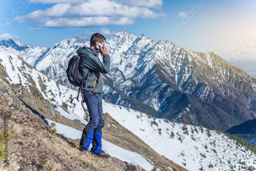 Young man with phone in hand on the top of a snowy mountain. Concept availability of mobile connection