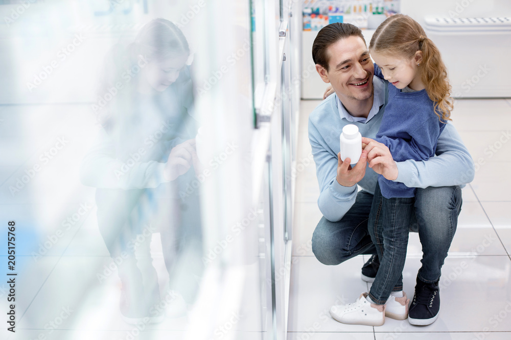 Healthy child. Nice beautiful girl staying while man elevating bottle with medication Healthy child. Nice beautiful girl staying while man elevating bottle with medication