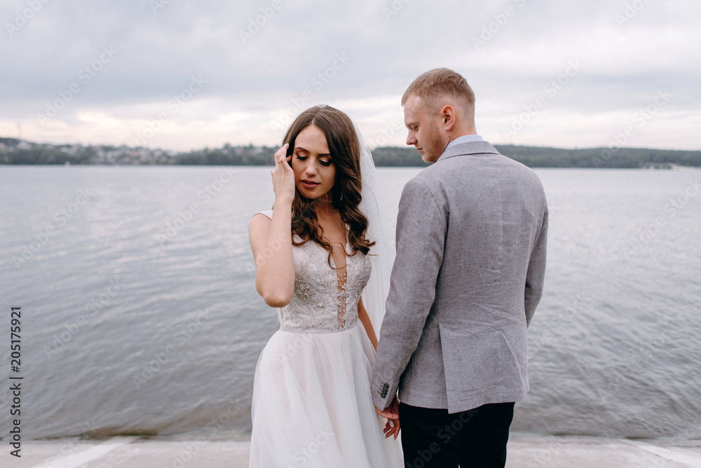 An amazing couple on their wedding day near the lake hug and enjoy each other. The bride and groom with a bouquet are happy together An amazing couple on their wedding day near the lake hug and enjoy each other. The bride and groom with a bouquet are happy together