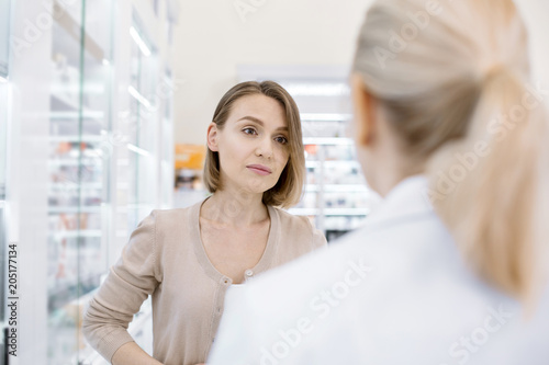 Health issue. Dismal dolorous woman posing on blurred background while communicating with female pharmacist