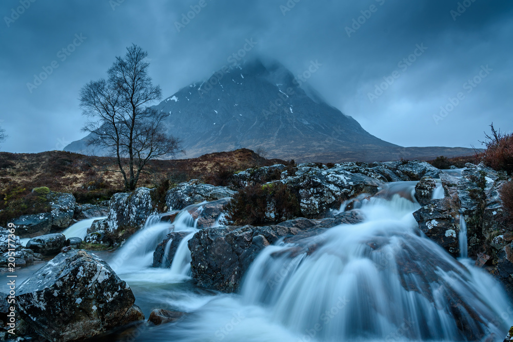 Beautiful panoramic image of the famous Etive Mor Waterfalls with silky smooth water, towering mountain and dark moody skies - typical Scottish landscape with breathtaking views and impressive scenery