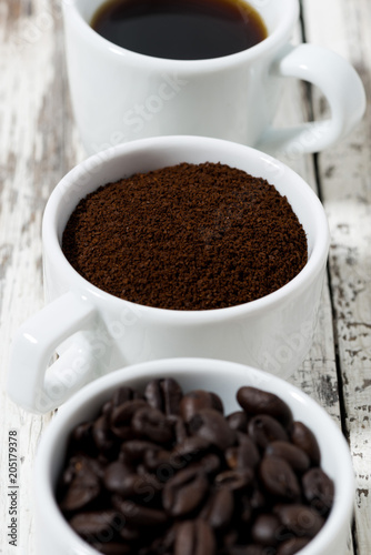 Three types of coffee - ground, grain and beverage in cups on white table, closeup