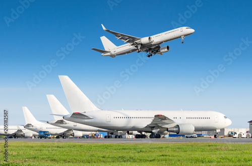 Passenger aircraft row, airplane parked on service before departure at the airport, other plane push back tow. Airplane landing to the runway in the blue sky.