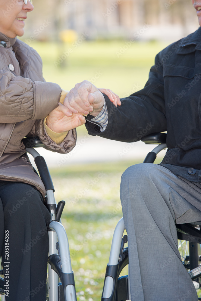 Closeup of hands of elderly couple in wheelchairs