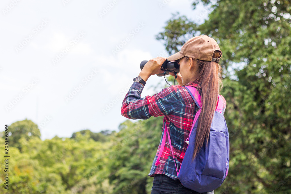 A female tourist sits on a rock using a binoculars to see the beautiful nature.