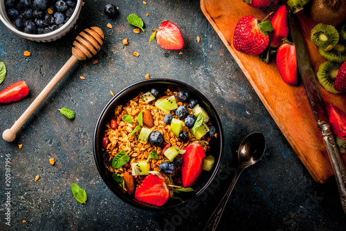 Healthy breakfast with muesli or granola with nuts and fresh berries and fruits - strawberry, blueberry, kiwi, on dark blue table, copy space top view