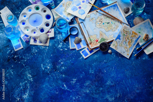 Artist workplace with a watercolor map, sketches, seashells and compass on a navy blue background with copy space. Travel flat lay header.