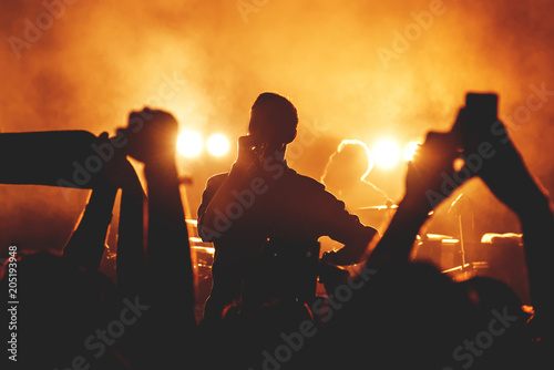 Silhouettes of people in a bright in the pop rock concert in front of the stage. Hands with gesture Horns. That rocks. Party in a club