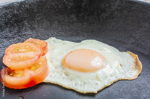 fried egg with tomatoes in a cast-iron frying pan on a wooden table