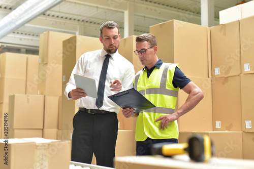 Arbeiter und Geschäftsmann bei einer Besprechung im Warenlager eines Versandhandels // Worker and businessman at a meeting in the warehouse of a mail-order company photo