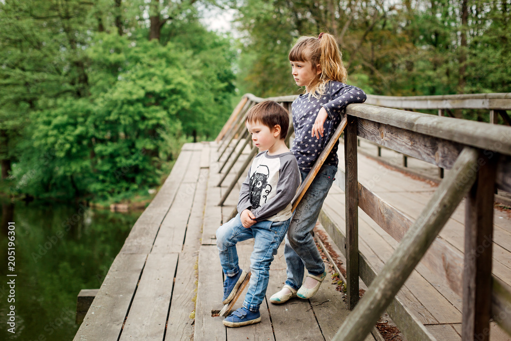Two little children, girl and boy, standing on the bridge of the river Two little children, girl and boy, standing on the bridge of the river