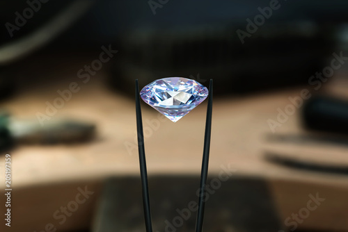 Beautiful diamond stone in tongs. Craft jewelery making with professional tools in jeweller studio. Macro shot.