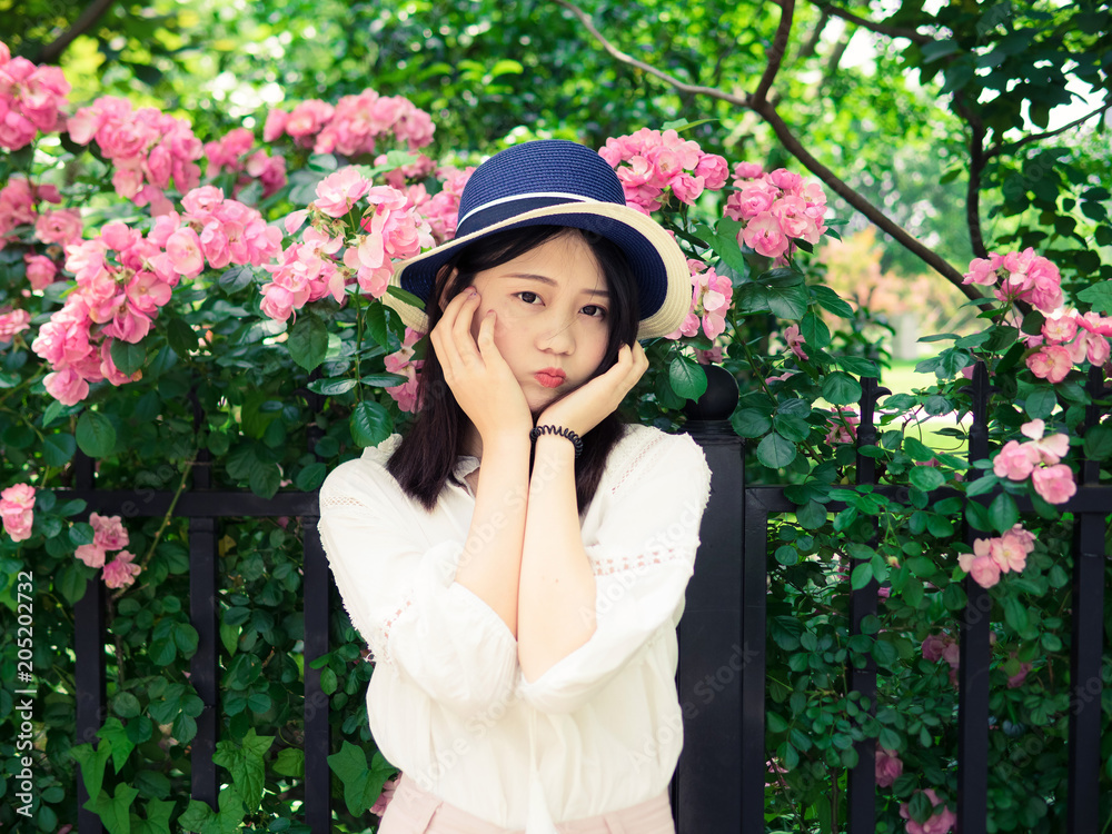 Outdoor portrait of beautiful young Chinese woman in casual dress smiling among pink rose flowers wall in spring garden. Outdoor portrait of beautiful young Chinese woman in casual dress smiling among pink rose flowers wall in spring garden.