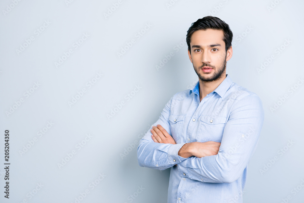 Portrait with copyspace empty place for advertisement of half-turned virile man with black hair holding arms crossed looking at camera isolated on grey background