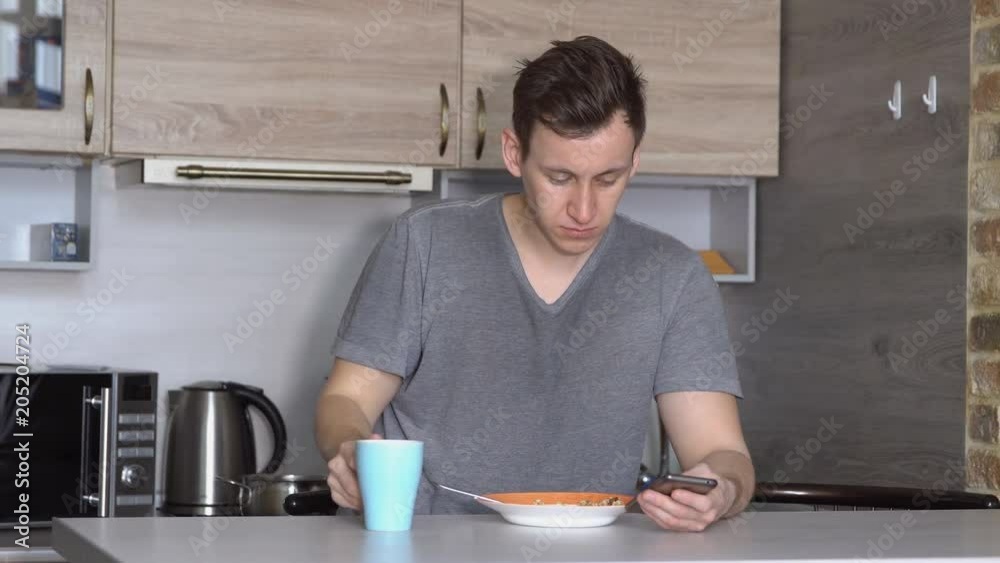 Young man with a phone eats at a table in the kitchen. Young man with a phone eats at a table in the kitchen.